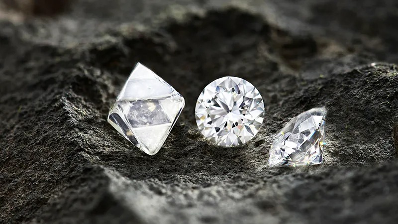 Natural diamond rough and polished stones on dark rock